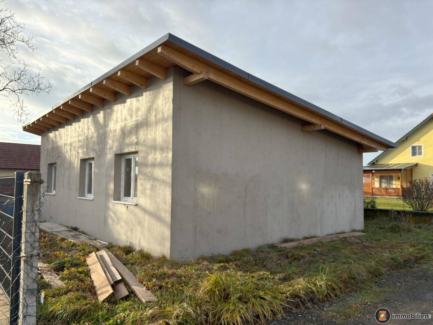 Seitenansicht des Neubaus mit mehreren Fenstern und dem sichtbaren Dachstuhl über dem grünen Rasen.