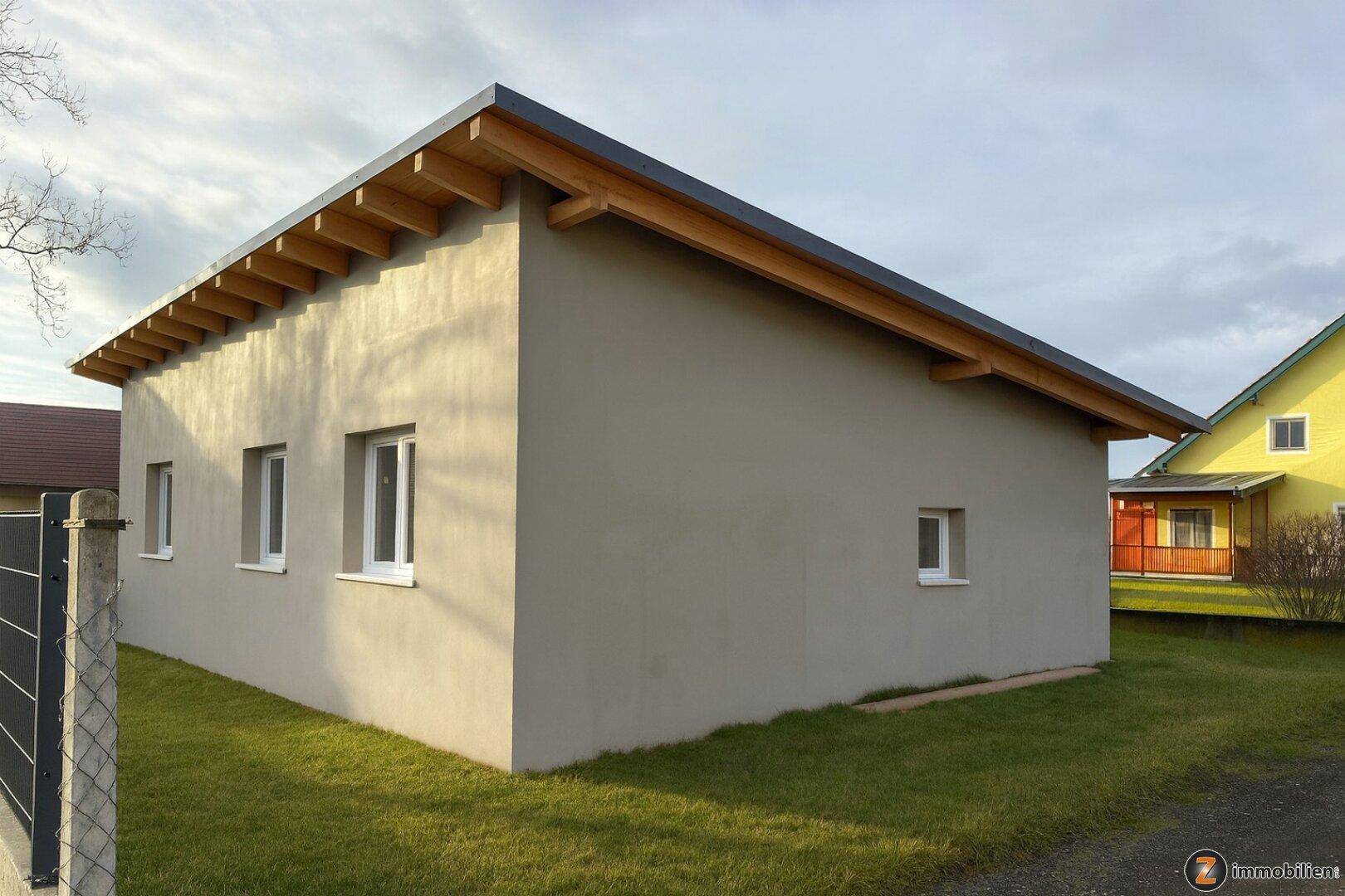 Seitenansicht des Neubaus mit mehreren Fenstern und dem sichtbaren Dachstuhl über dem grünen Rasen.