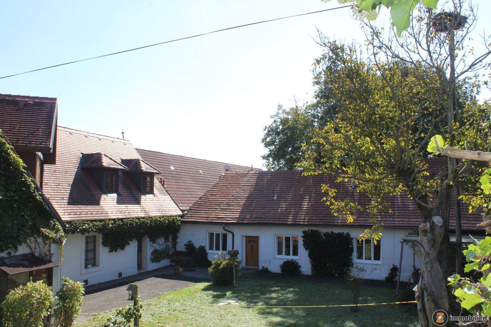 Traditionelles Landhaus mit rotem Ziegeldach, weißer Fassade und begrüntem Vorgarten.