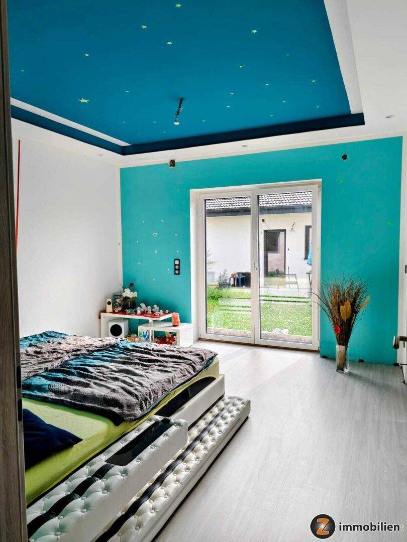 Schlafzimmer mit farbiger Wandgestaltung, Deckenbeleuchtung und Zugang zum Garten.