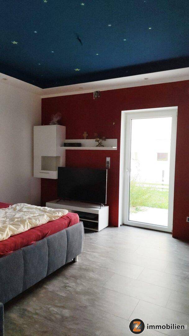 Schlafzimmer mit roter Akzentwand, Fernseher und Zugang zum Außenbereich.