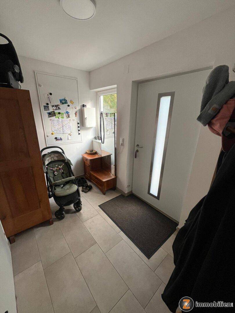 Heller Eingangsbereich mit Fliesenboden, Garderobe und einer modernen Haustür mit Glaseinsatz.