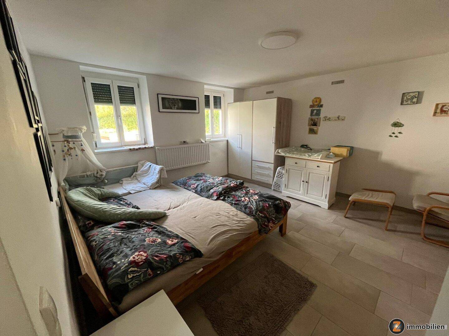 Helles Schlafzimmer mit Fliesenboden, Doppelbett und weißem Kleiderschrank, gut gepflegt.