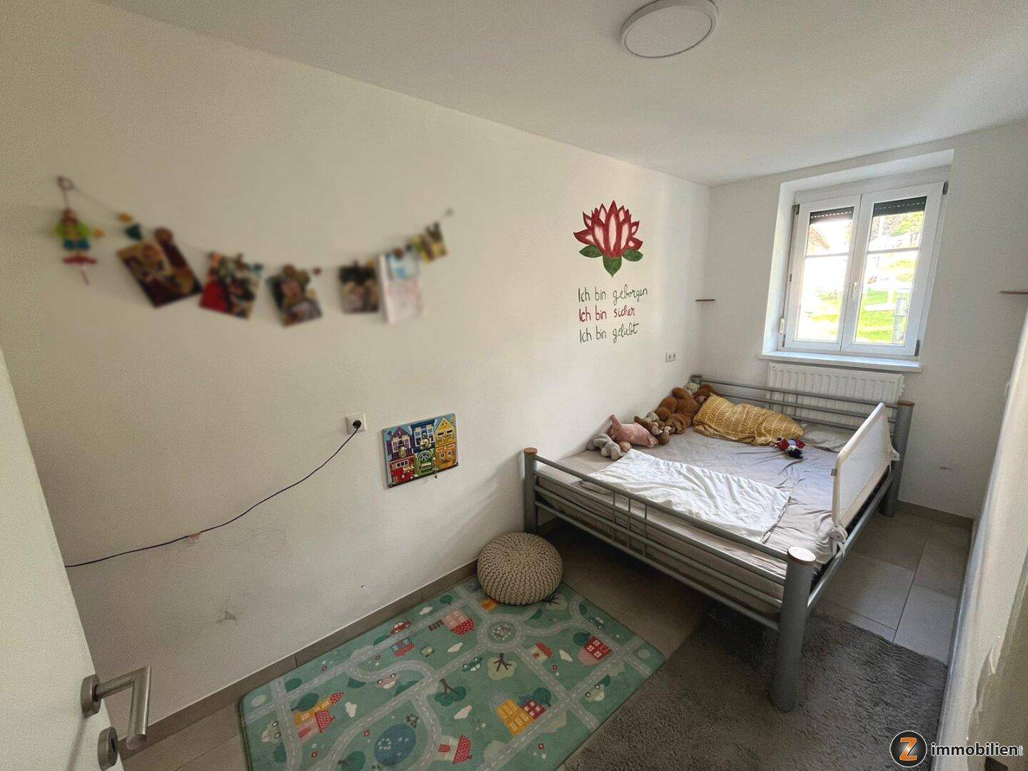Kinderzimmer mit Fliesenboden, Einzelbett und farbenfroher Wanddekoration, hell und freundlich.