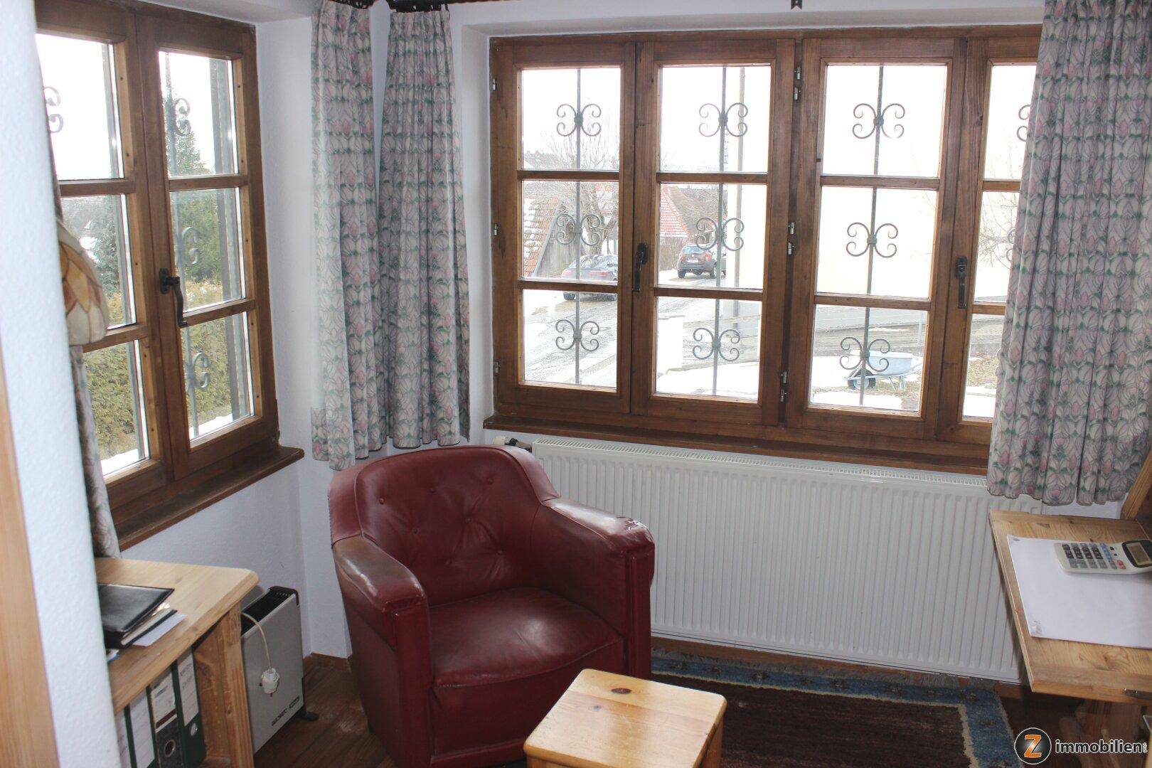 Kleines Arbeitszimmer mit Holzboden, rotem Sessel und Blick auf die verschneite Straße.