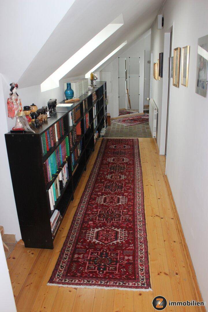 Langer Flur im Dachgeschoss mit Bücherregalen, Holzboden und Dachschrägen.