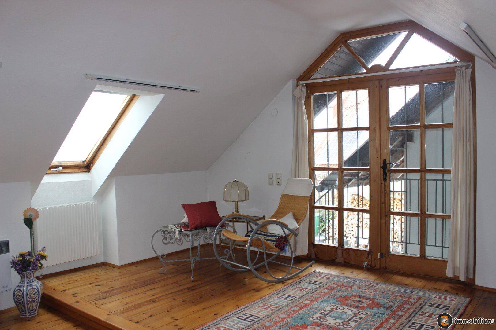 Gemütlicher Lesebereich im Dachgeschoss mit Holzboden, Dachfenster und Zugang nach draußen.