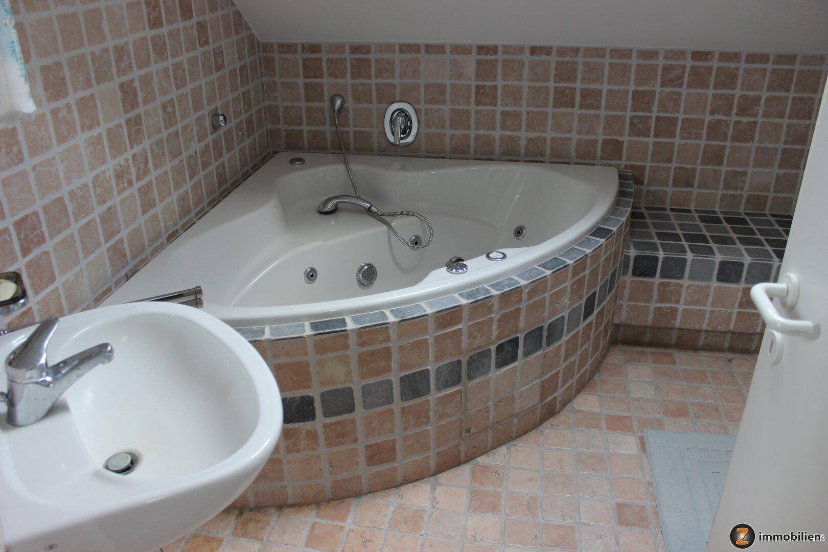 Badezimmer mit Eckbadewanne, Bidet und braunen Mosaikfliesen.