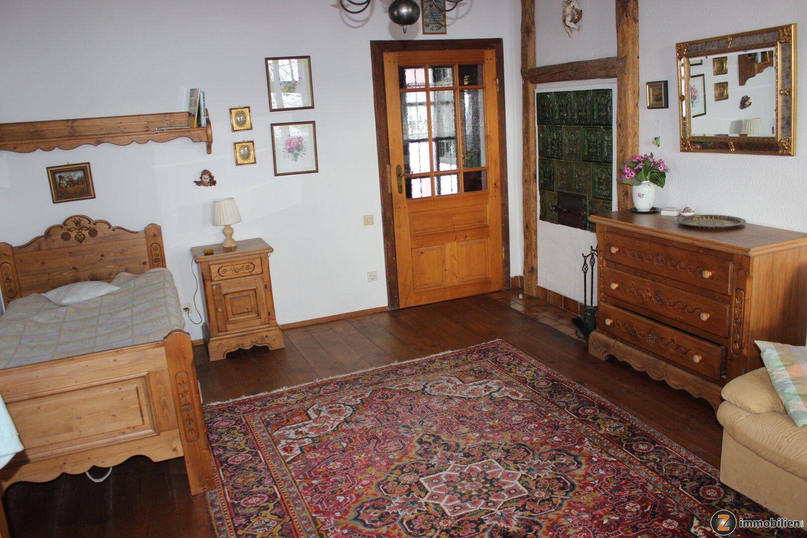 Schlafzimmer mit Holzboden, traditionellem Bett und grünem Kachelofen.