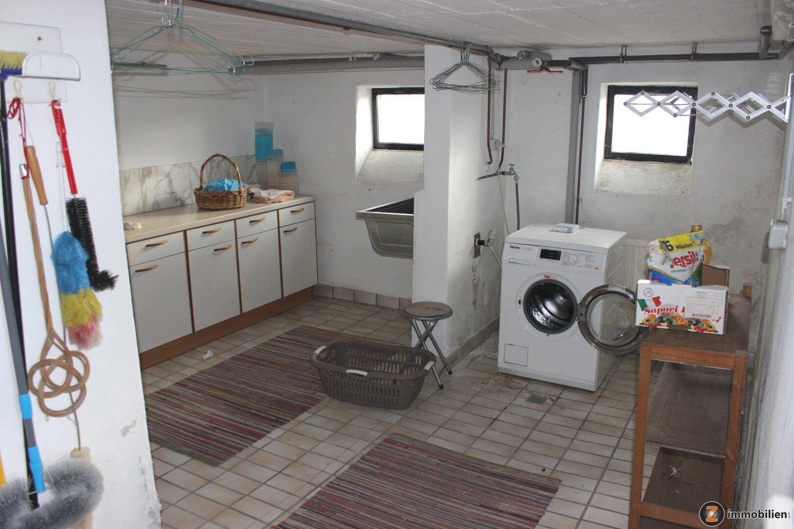 Praktischer Waschraum im Keller mit Waschmaschine, Spülbecken und Fliesenboden.