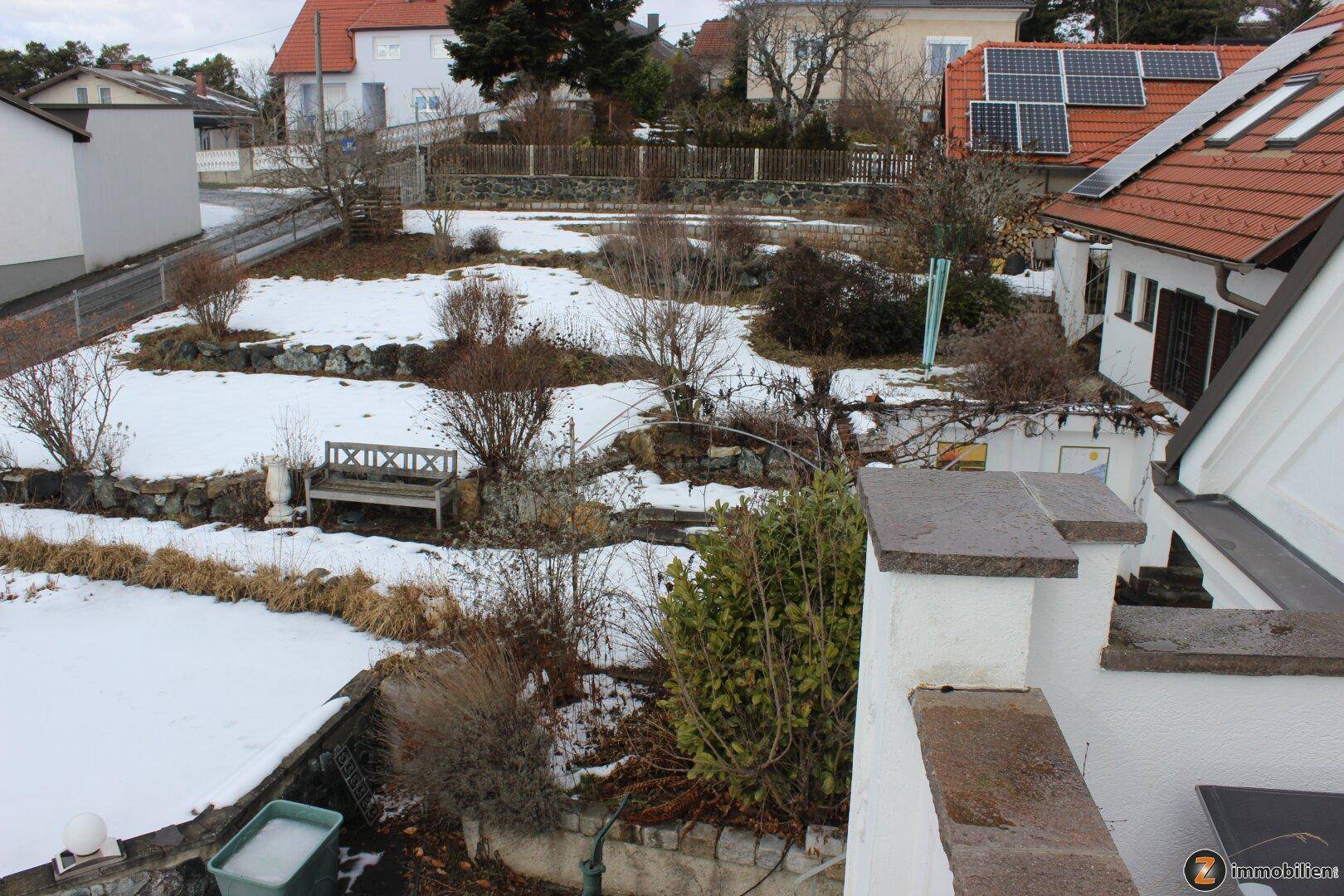 Terrassierter Gartenbereich mit Sitzbank und Blick auf die verschneite Umgebung.