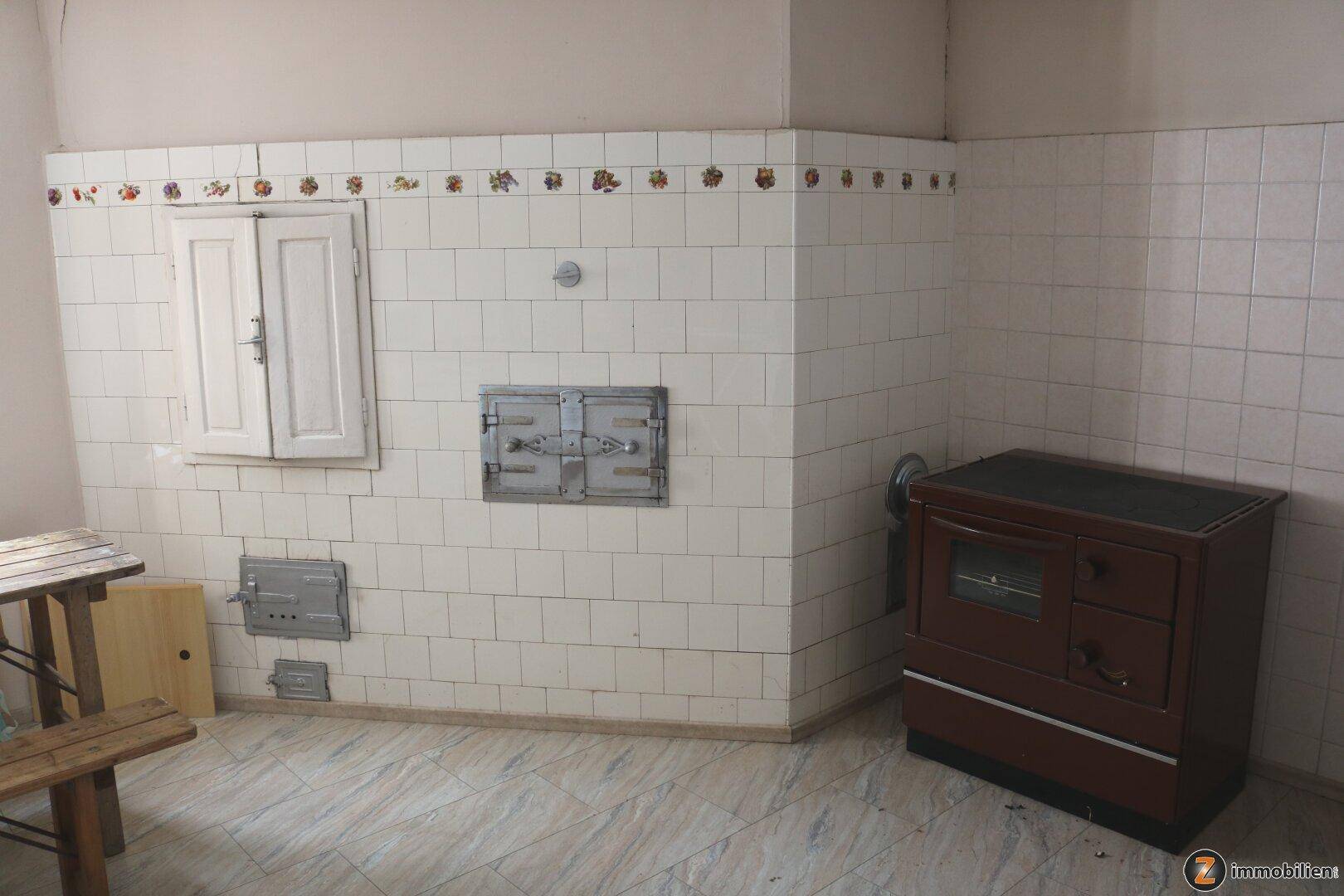 Traditionelle Küche mit gefliesten Wänden, altem Holzofen und rustikalem Holztisch.