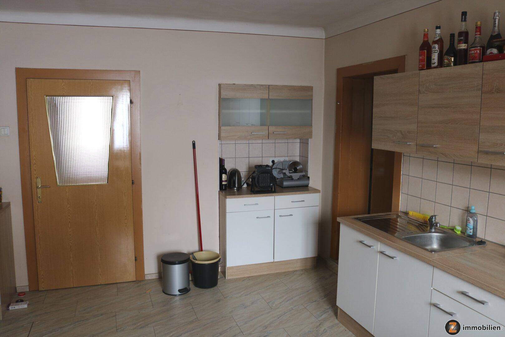 Einfache Küchenzeile mit Spüle, Oberschränken und hellem Fliesenboden.