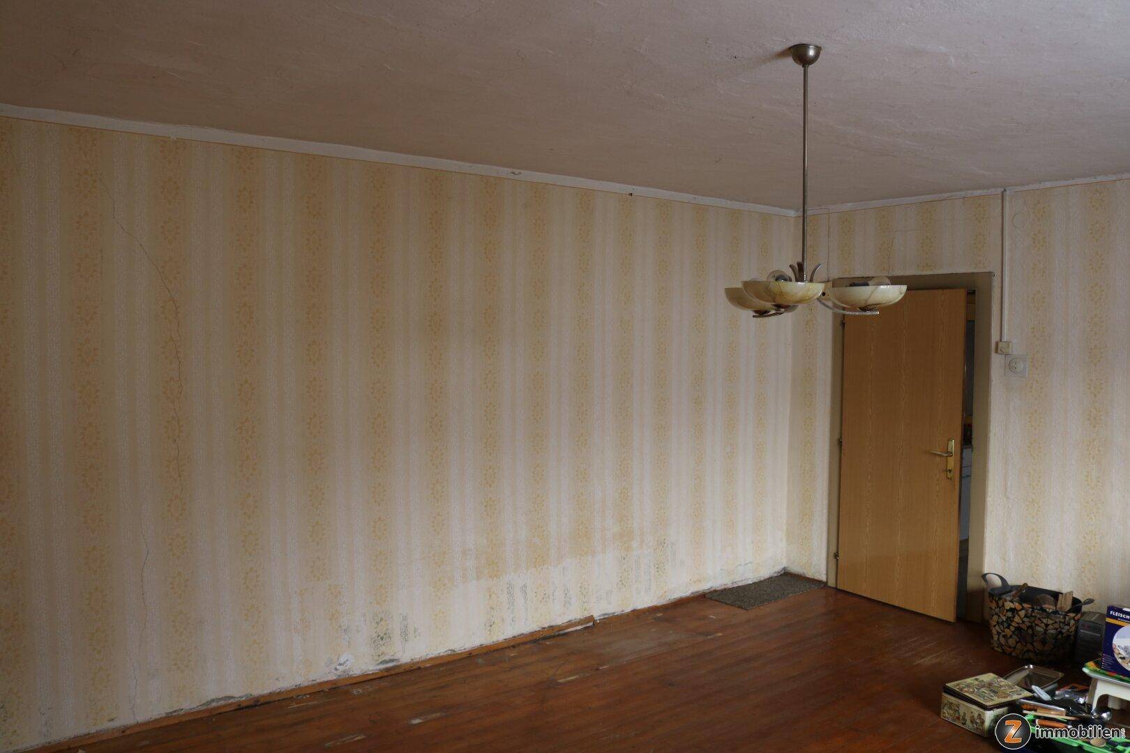 Geräumiger Raum mit Holzboden, gestreifter Tapete und einfacher Deckenleuchte.