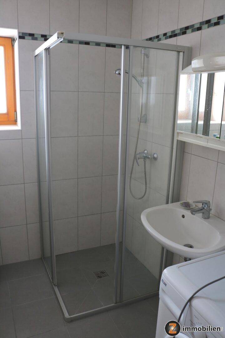 Helles Badezimmer mit Duschkabine, Waschbecken und Fenster, einfach gefliest.