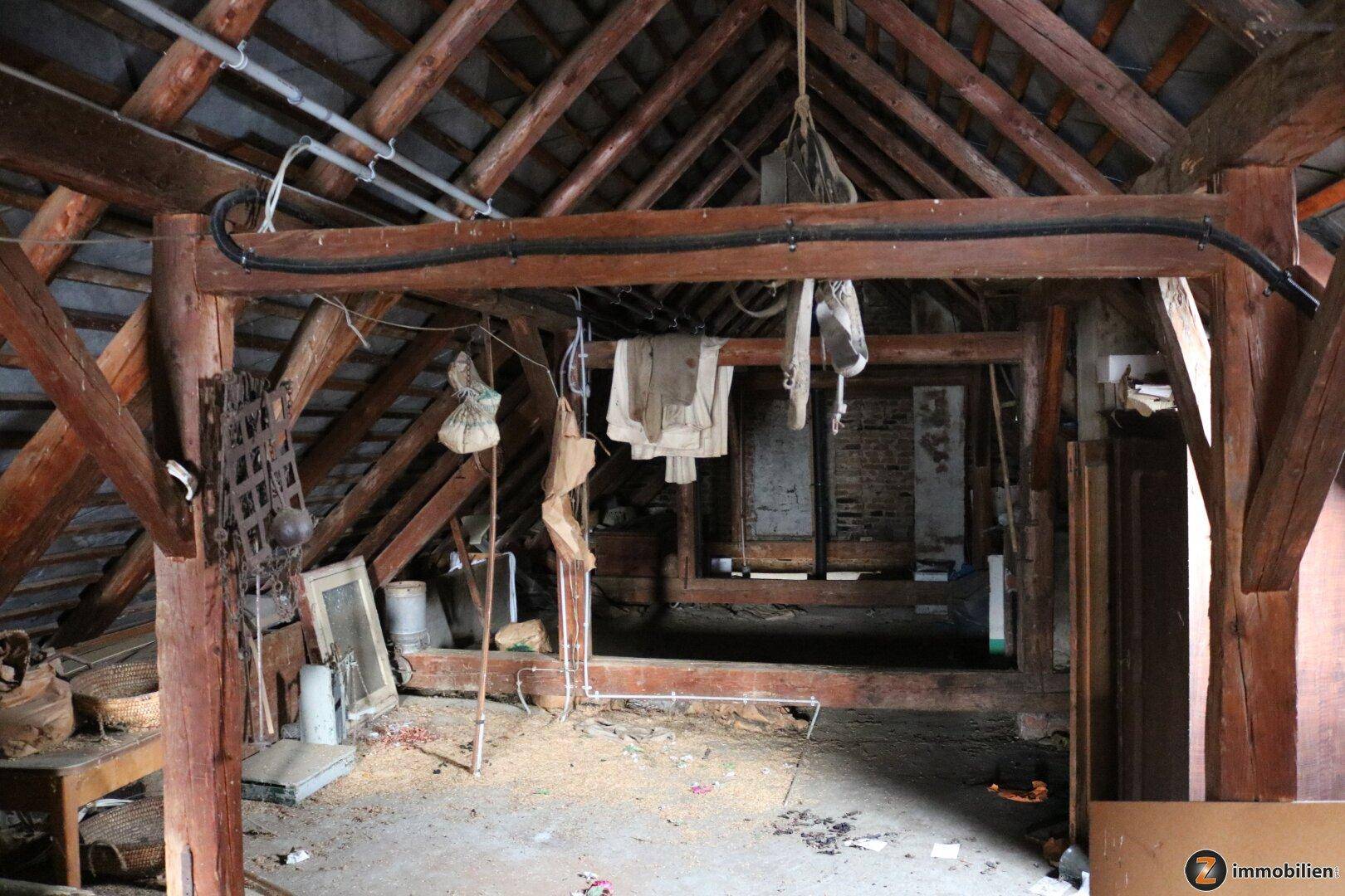Geräumiger Dachboden mit sichtbaren Holzbalken und gelagerten Gegenständen, viel Potenzial.