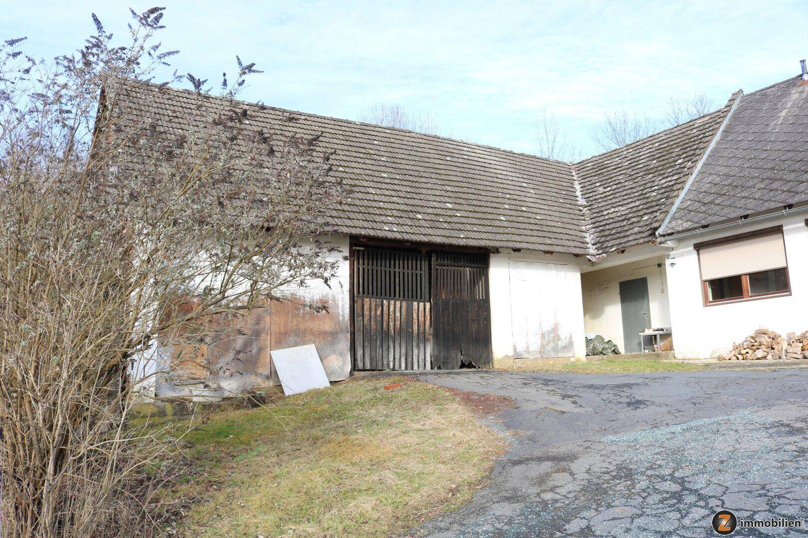 Eingangsbereich der großen Scheune oder des Lagergebäudes mit Holztoren und Zufahrt.