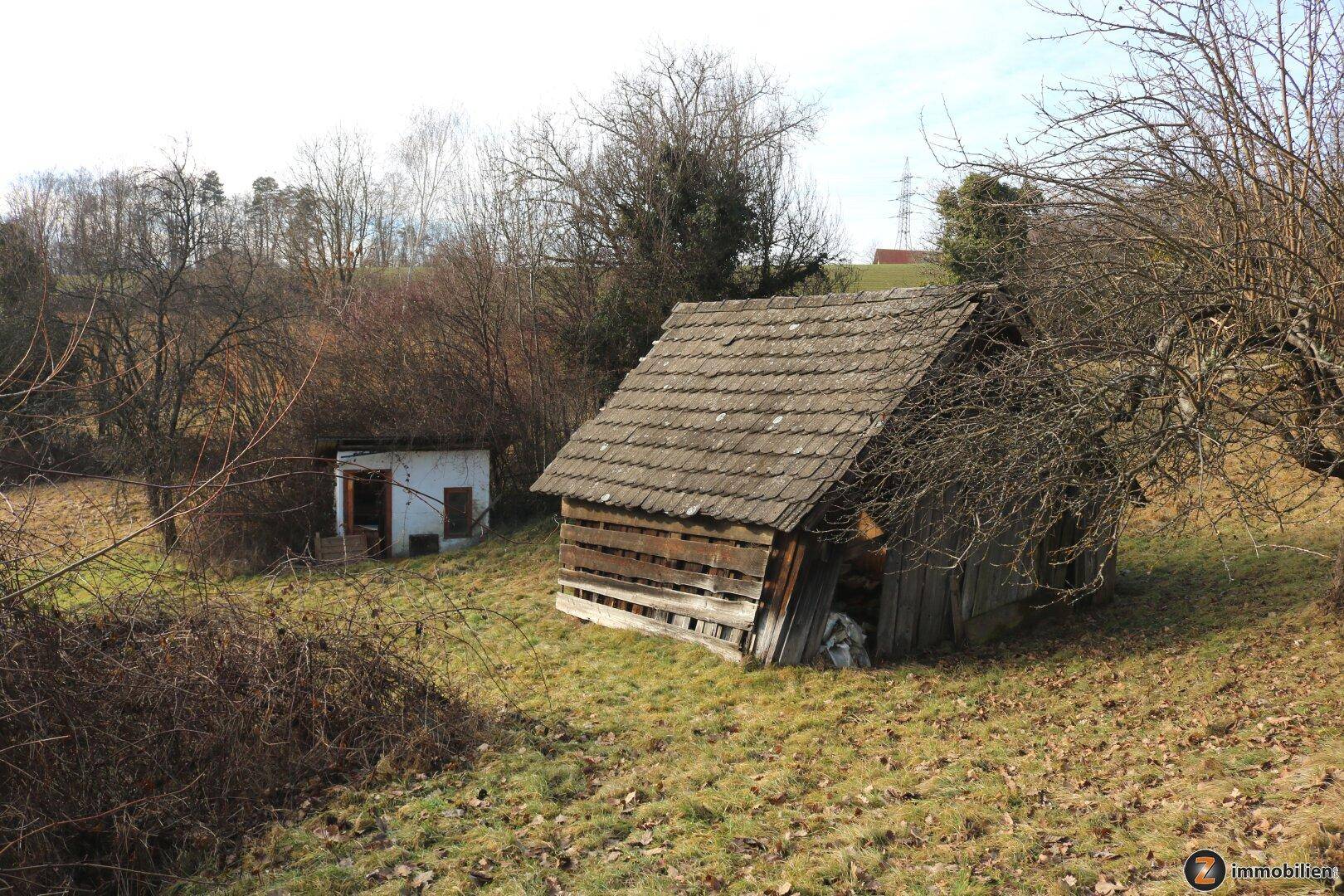Rustikale Holzscheune und kleines Nebengebäude auf dem weitläufigen, grasbewachsenen Grundstück.