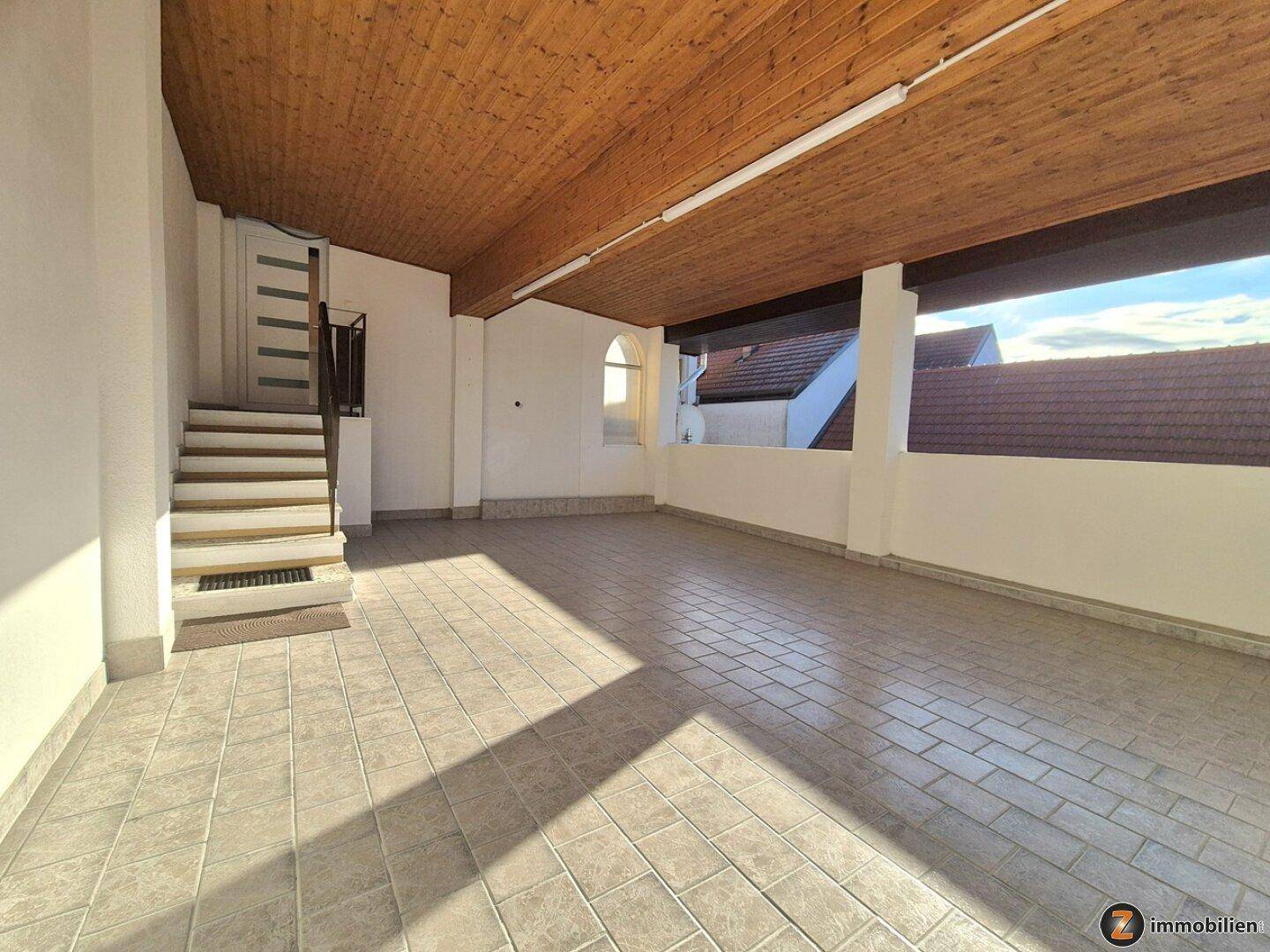 Überdachter Außenbereich mit Fliesenboden und Holzdecke, ideal als geschützter Stellplatz oder Freisitz.