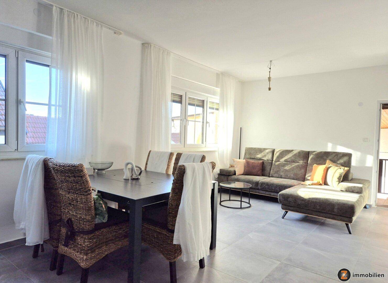 Geräumiger Wohn- und Essbereich mit bequemer Couch, Esstisch und großen Fenstern für viel Licht.