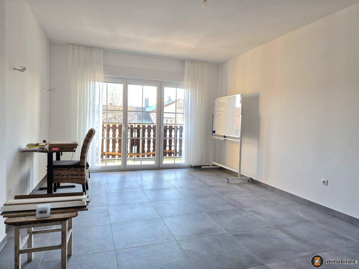 Geräumiger Raum mit Fliesenboden und direktem Zugang zu einem Balkon durch große Glastüren.