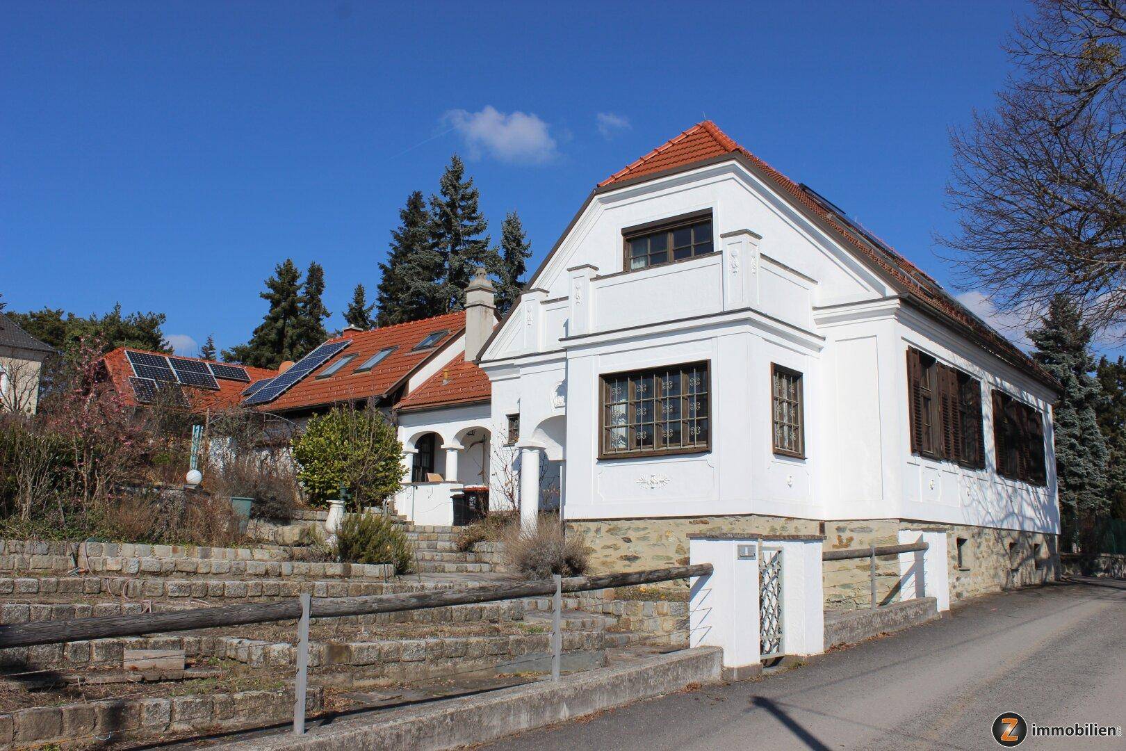 Ansicht des Wohnhauses von der Straße mit weißer Fassade, Ziegeldach und gepflegter Umgebung.