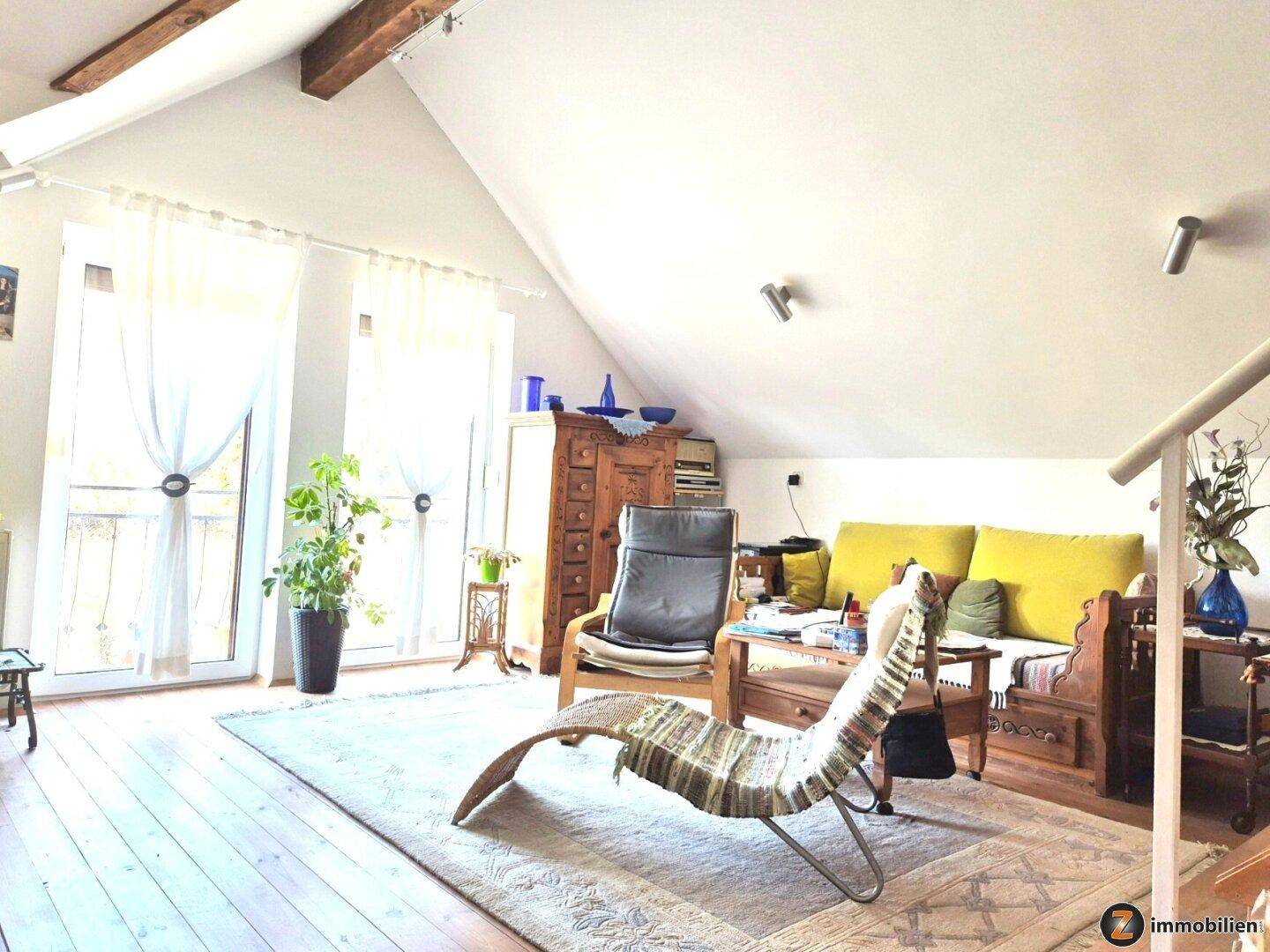 Helles Wohnzimmer im Dachgeschoss mit Holzbalken, bequemen Sitzgelegenheiten und viel Tageslicht.