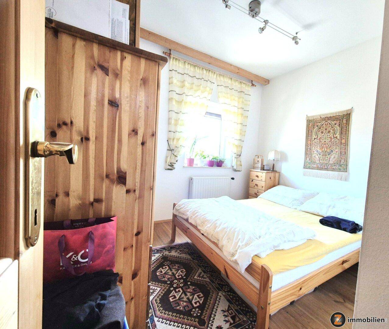Gemütliches Schlafzimmer mit Holzboden, Holzbett und Fenster mit Vorhängen.