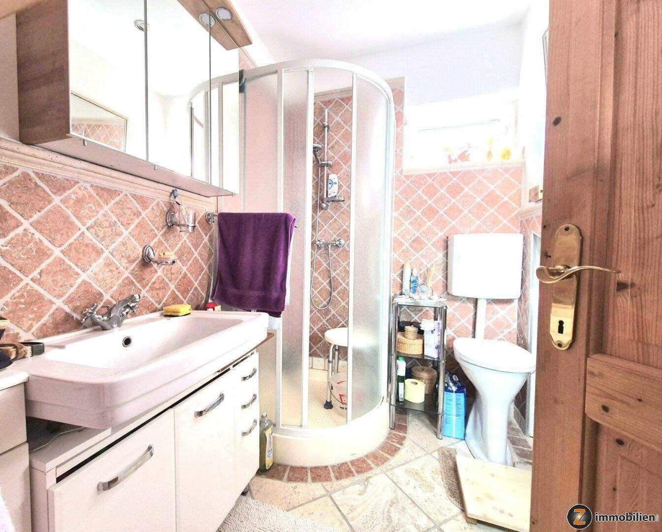 Badezimmer mit Duschkabine, Waschbecken und WC, ausgestattet mit gemusterten Fliesen.