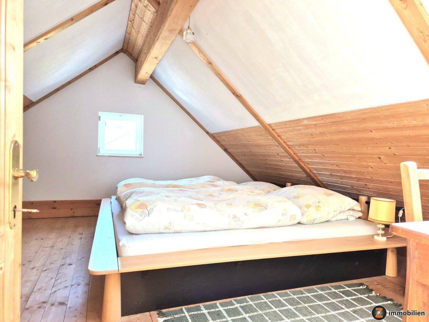 Schlafzimmer im Dachgeschoss mit Holzbalken, Holzwänden und einem kleinen Fenster.
