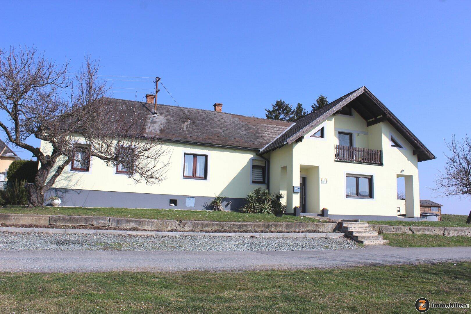 Gelb gestrichenes Einfamilienhaus mit Satteldach und kleinem Balkon, umgeben von Grünflächen.