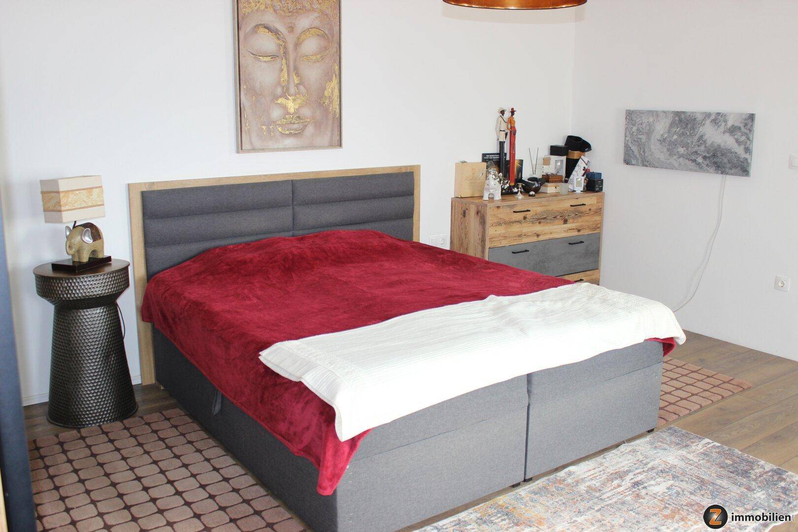 Schlafzimmer mit großem Doppelbett, Holzboden und moderner Einrichtung in warmen Farbtönen.