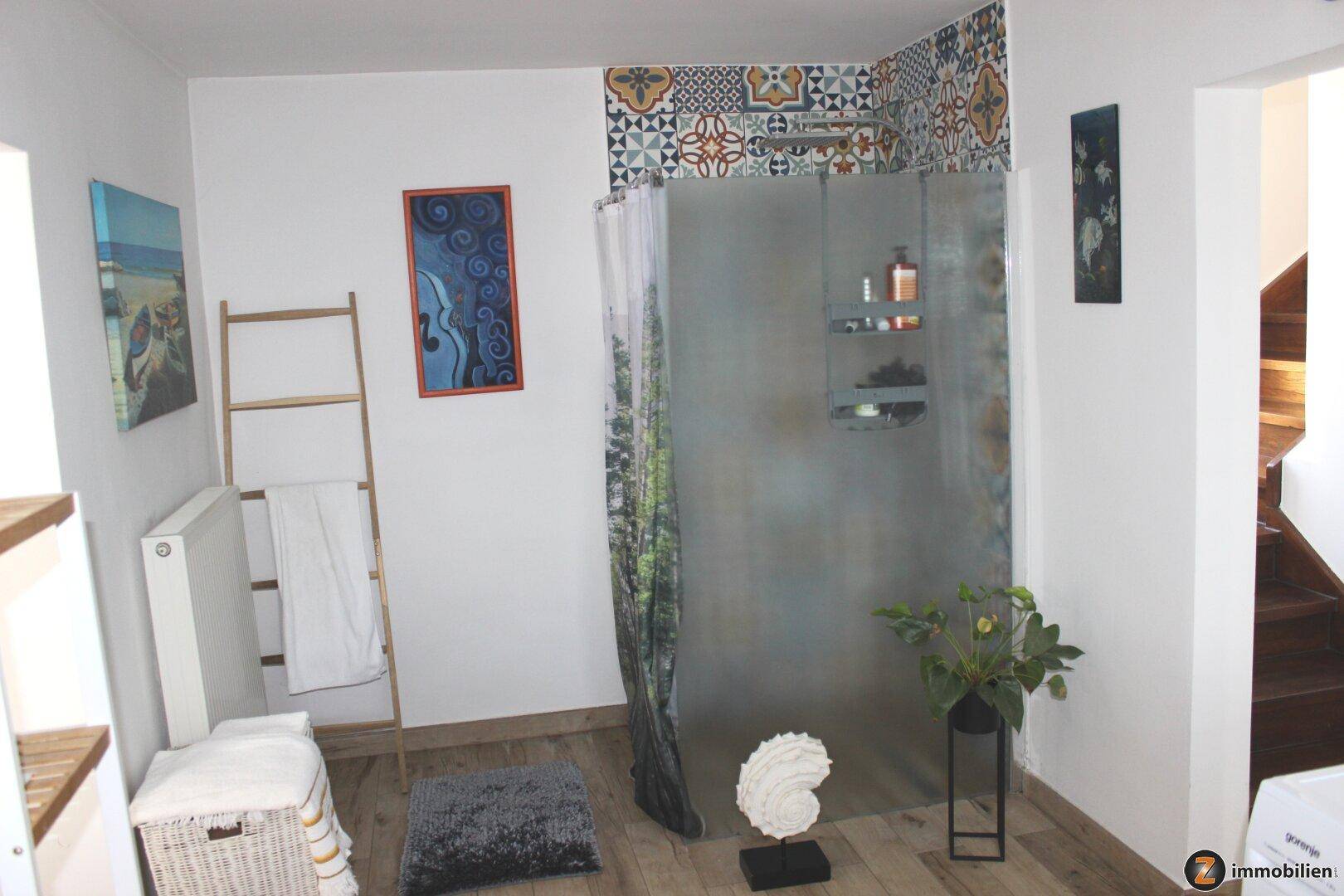 Badezimmer mit geräumiger Duschkabine, bunten Fliesen und Holzboden, hell und freundlich.