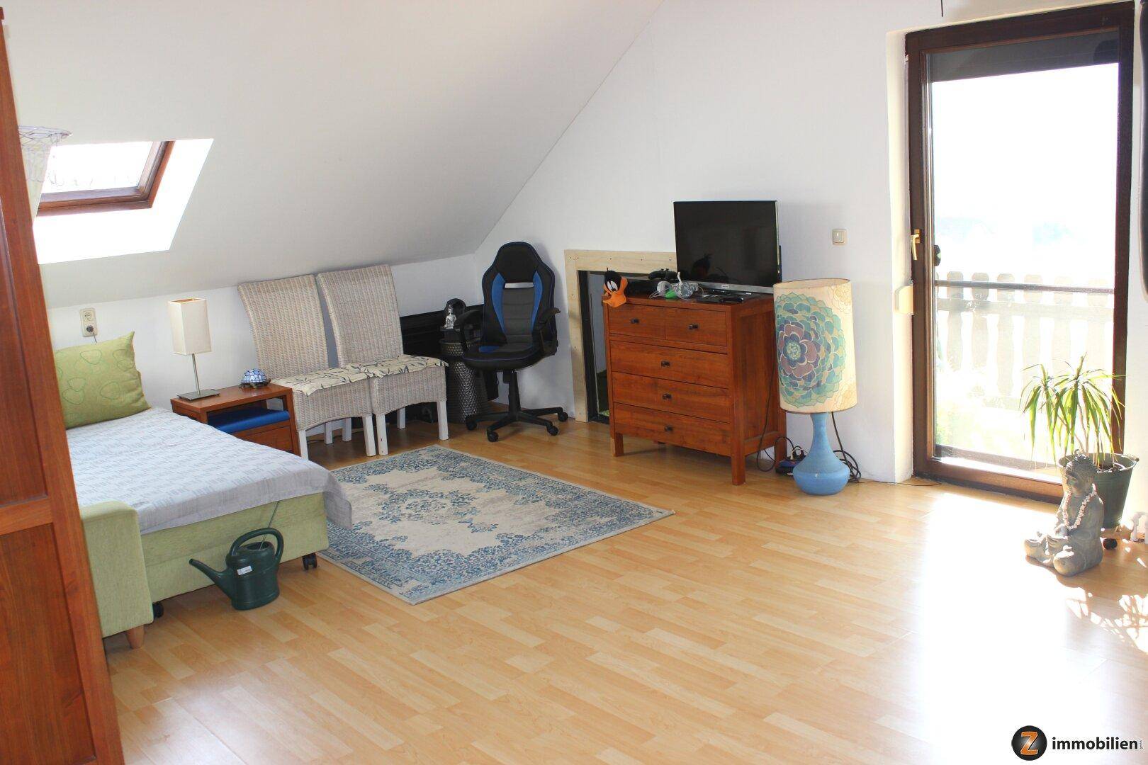 Helles Dachgeschosszimmer mit Laminatboden, Dachschräge und Zugang zu einem kleinen Balkon.
