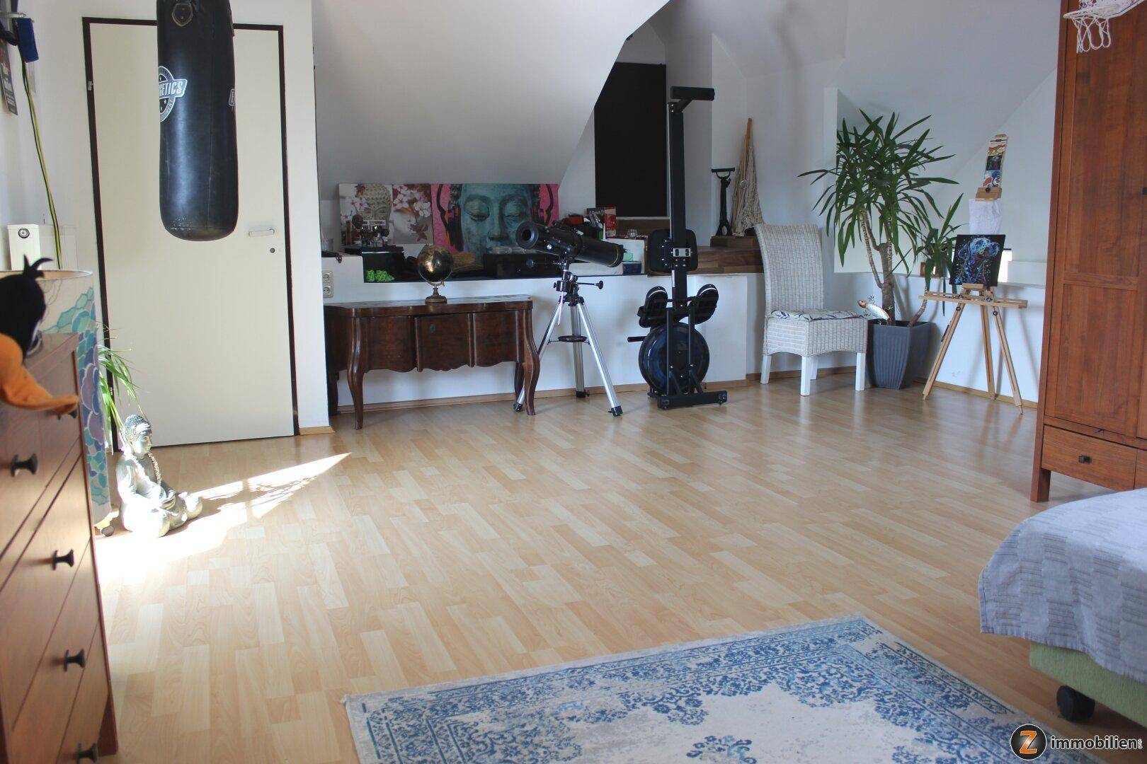 Geräumiges Dachgeschosszimmer mit Laminatboden, Fitnessgeräten und vielseitiger Nutzungsmöglichkeit.