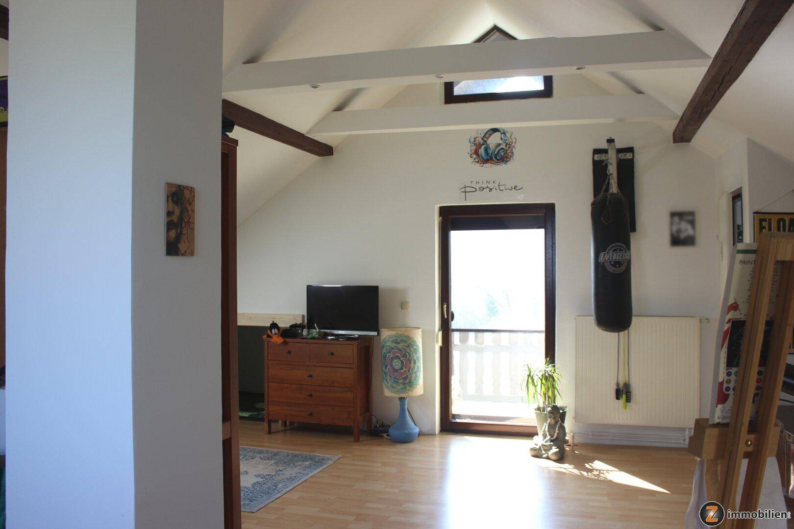 Helles Dachgeschosszimmer mit Holzbalken, Laminatboden und Zugang zu einem Außenbereich.