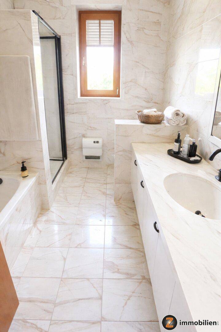 Modernes Badezimmer mit Marmorfliesen, Dusche und Badewanne, sowie einem Fenster für Tageslicht.