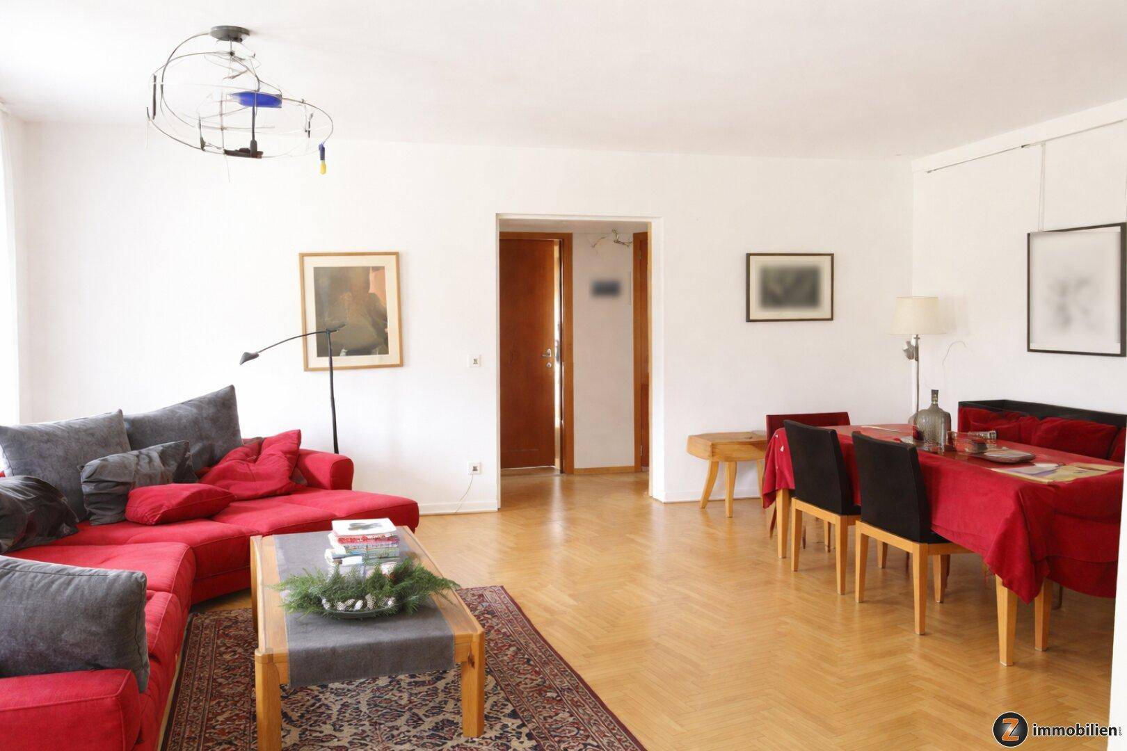 Geräumiger Wohn-Essbereich mit Parkettboden, rotem Sofa und Esstisch für gesellige Stunden.