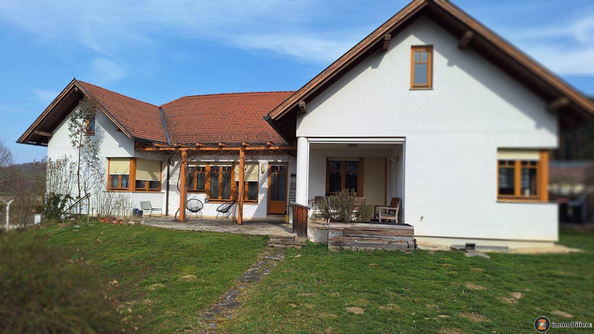 Freistehendes Haus mit großem Garten, überdachter Terrasse und Holzpergola unter blauem Himmel.