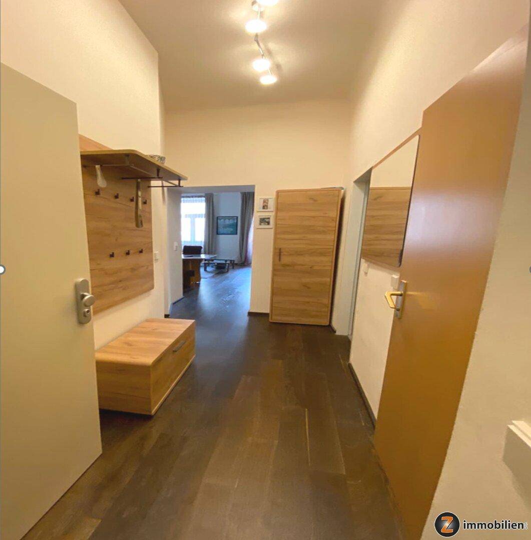 Heller Flur mit dunklem Holzboden, Garderobe und Spiegel, der zu den weiteren Wohnbereichen führt.