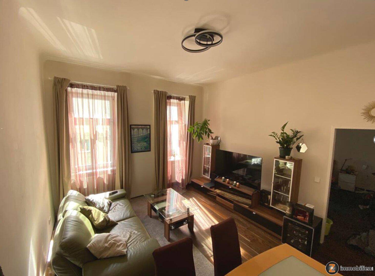 Heller Wohnbereich mit bequemer Couch, Couchtisch und Unterhaltungselektronik, durchflutet von Sonnenlicht.