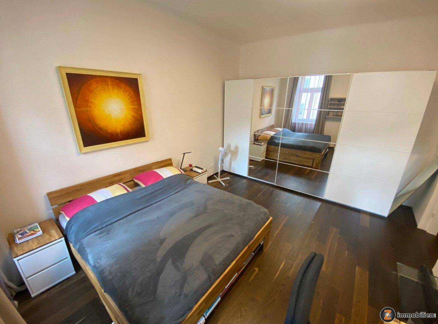 Gemütliches Schlafzimmer mit Doppelbett, großem Spiegelschrank und dunklem Holzboden, hell und einladend.
