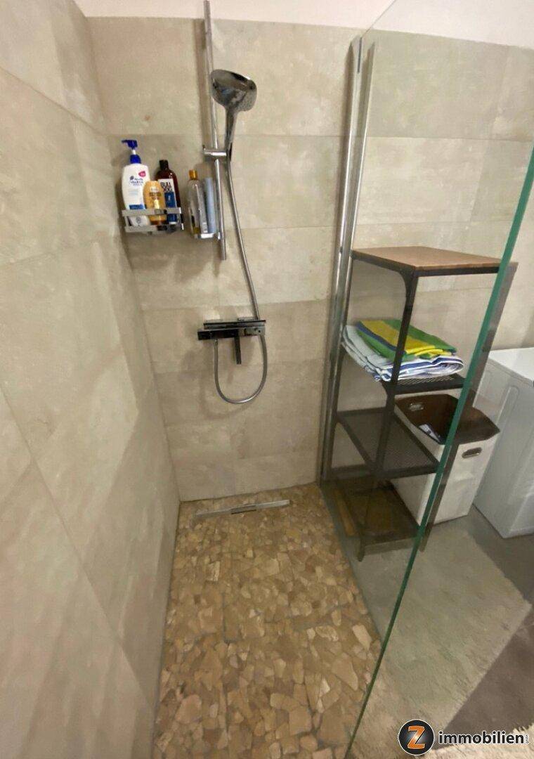 Moderne Duschkabine mit Fliesenwänden und Glasabtrennung, ausgestattet mit einer praktischen Ablage.