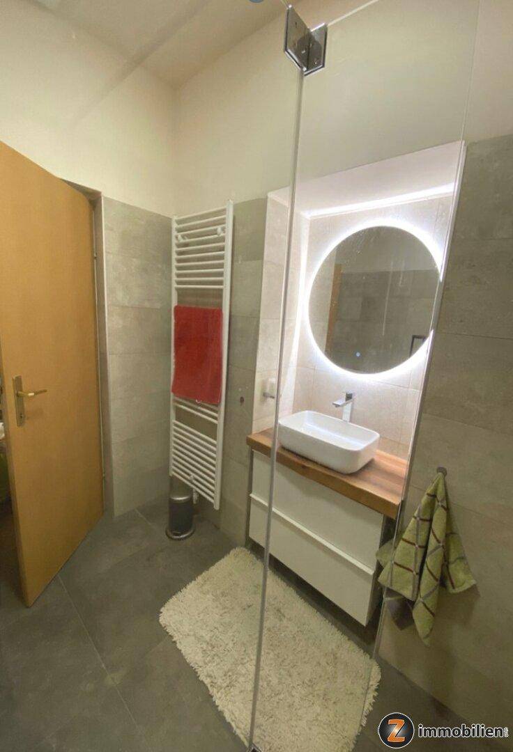 Modernes Badezimmer mit stilvollem Waschtisch, beleuchtetem Spiegel und beheiztem Handtuchhalter, sehr gepflegt.