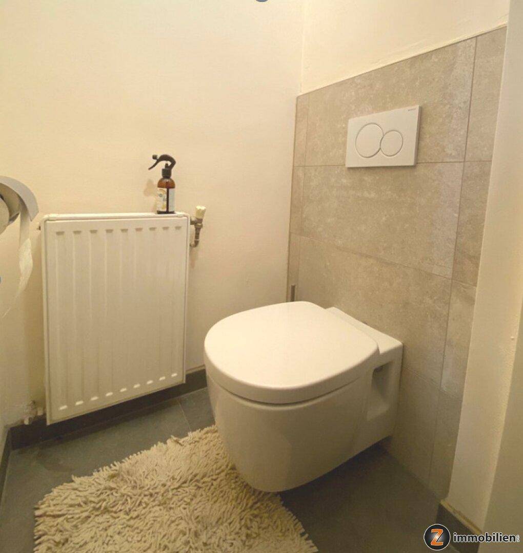 Separates WC mit wandhängender Toilette und Heizkörper, modern gefliest und sauber.