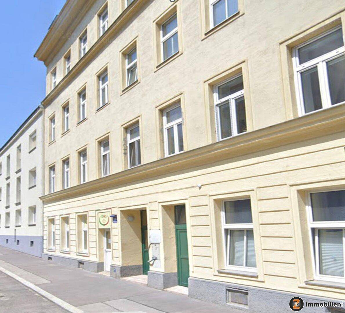Historische Fassade eines Mehrfamilienhauses mit gelbem Putz und klassischen weißen Fenstern an einer ruhigen Straße.