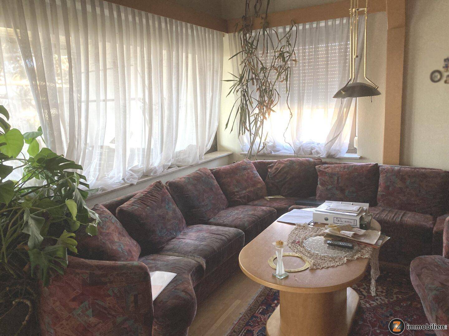 Gemütliches Wohnzimmer mit großer Eckcouch, Couchtisch und Vorhängen vor den Fenstern.