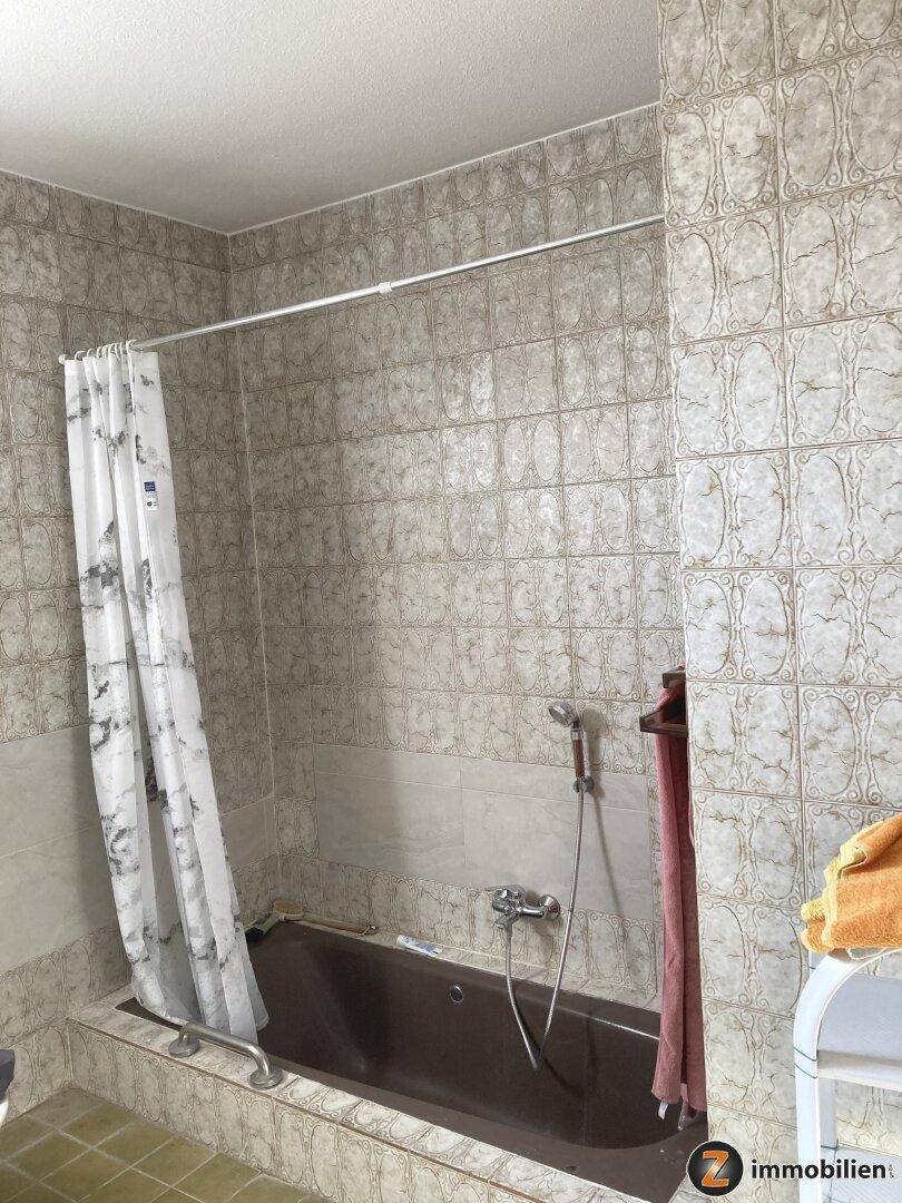 Badezimmer mit Badewanne, Duschvorhang und gemusterten Fliesen in hellen Tönen.