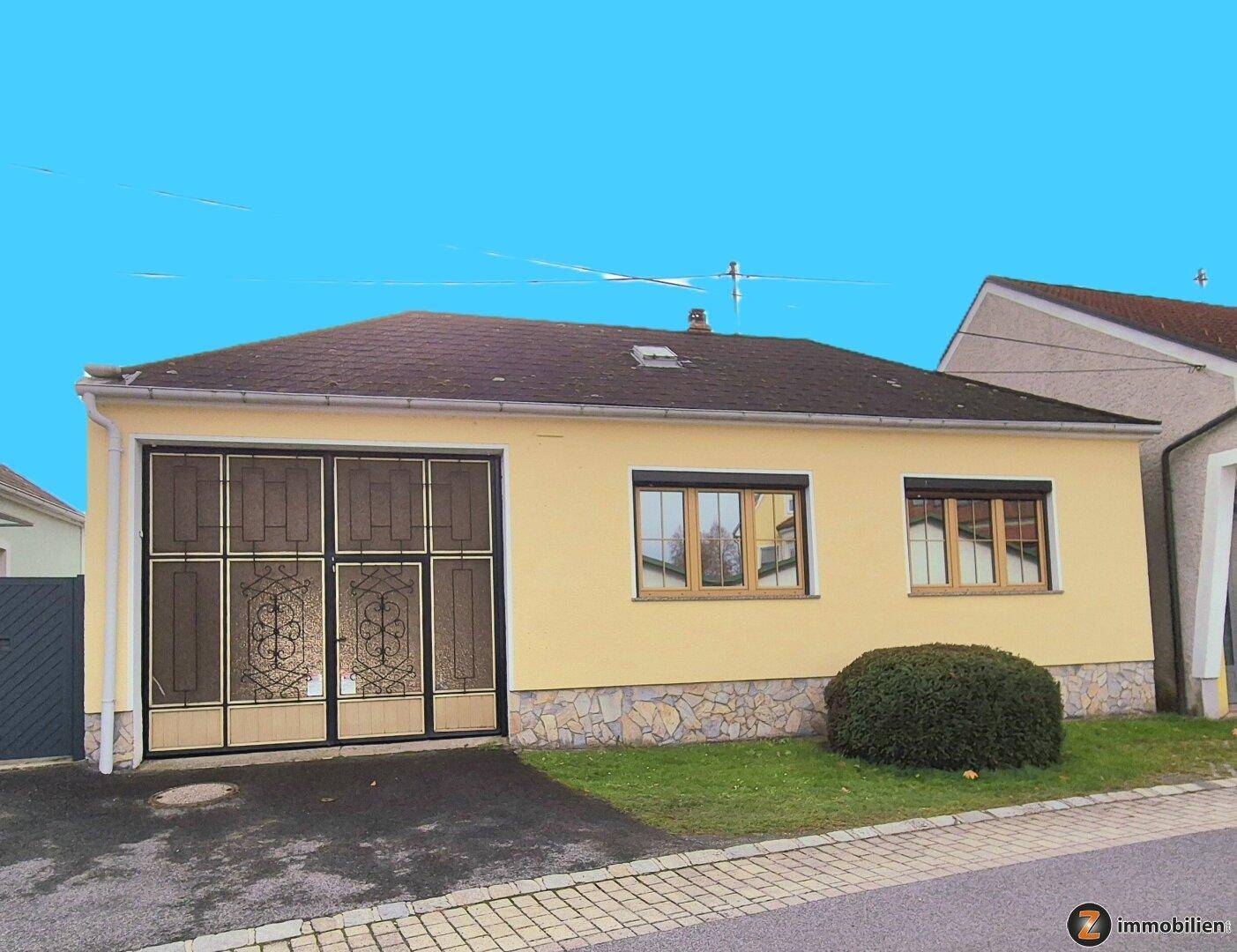 Gelbes Einfamilienhaus mit Garagentor und kleinen Fenstern, umgeben von einem gepflegten Vorgarten.