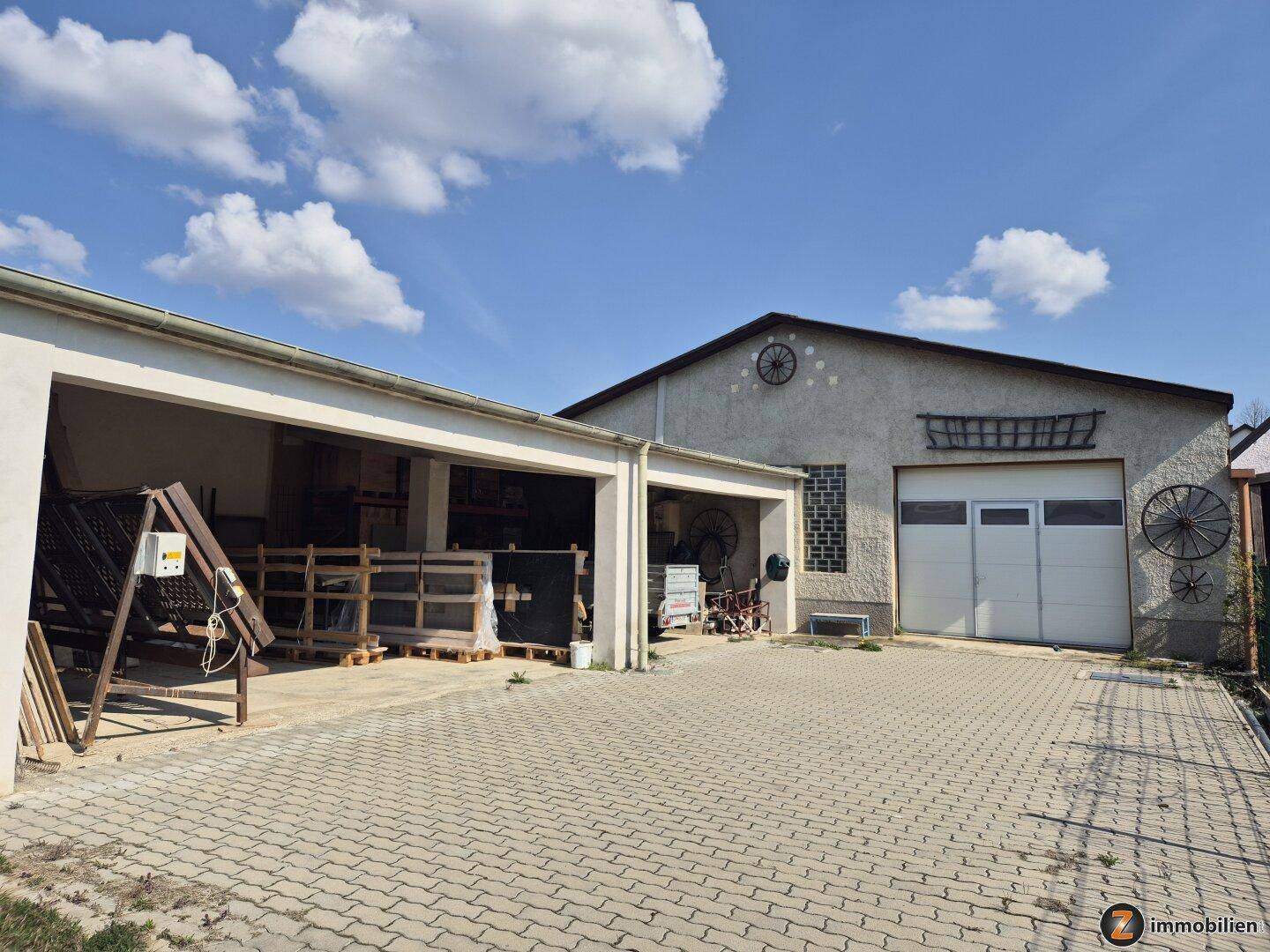 Außenansicht einer Garage und eines Werkstattgebäudes mit gepflastertem Vorplatz.